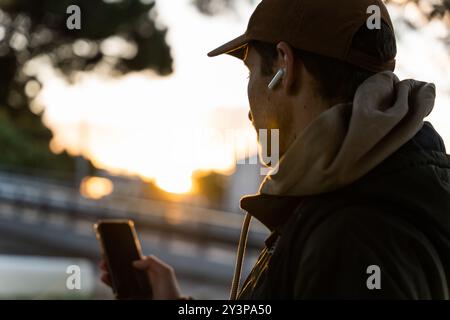 Ein 30-jähriger Mann spaziert an einem Herbstnachmittag durch die Stadt und schaut auf sein Smartphone Stockfoto