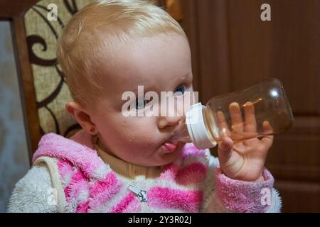 Das Baby im Speisesaal trinkt Wasser aus einer Flasche Stockfoto