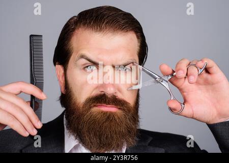 Bärtiger Mann, bärtiger Mann. Porträt eines stilvollen Mannes mit Friseurschere und Friseurkamm im Friseurladen. Bärtiger Kunde besucht Friseurladen. Bär Stockfoto