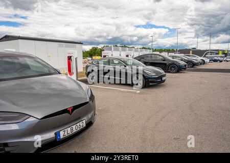 Halmstad, Schweden - 10. Juli 2022: Lange Reihe von Tesla-Autos laden am Tesla Supercharger Halmstad auf. Stockfoto
