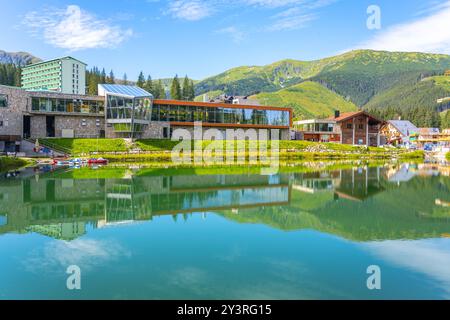 Das ruhige Wasser spiegelt die landschaftliche Schönheit des Jasna Ski Resort in der Niederen Tatra wider. Lebhaftes Grün und moderne Architektur schaffen eine malerische Sommerlandschaft für Besucher. Stockfoto