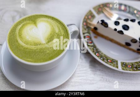 matcha Drink in einem weißen Becher und Dessert mit Heidelbeeren auf einer Café-Terrasse im Sommer Stockfoto