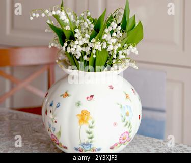 Blumenstrauß von Maiglöckchen in weißer Vase drinnen auf dem Tisch. Frühlingsblumen und Stimmung, Lebensstil. Stockfoto