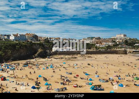 Eine lebhafte Strandszene mit zahlreichen bunten Sonnenschirmen und Sonnenanbetern an einem Sandstrand. Im Hintergrund befindet sich eine Küstenstadt mit Gebäuden und Klippen Stockfoto