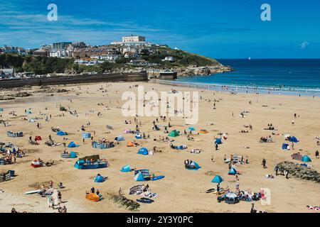 Eine lebhafte Strandszene mit zahlreichen Menschen, die die Sonne genießen. Bunte Sonnenschirme und Handtücher sind am Sandstrand verstreut, während einige indi sind Stockfoto