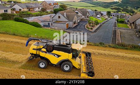 Kombinieren Sie Harvester Gardenstown Aberdeenshire Schottland einige Dorfhäuser und einen Erntemaschine auf dem Feld im Spätsommer Stockfoto