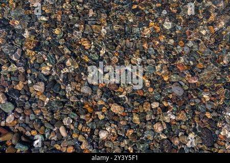 Schöne Steine am Boden sind durch das transparente Wasser sichtbar. Spiel von Licht und Reflexionen. Ein skurriler natürlicher Hintergrund. Stockfoto