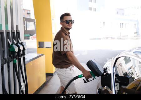 Gutaussehender Mann, der sein Luxusauto an einer Selbstbedienungstankstelle betankt. Benzinbefüllung an der Tankstelle im Auto mit einer Kraftstoffdüse. Stockfoto