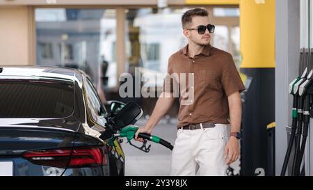 Gutaussehender Mann in Sonnenbrille, der sein Auto an der Selbstbedienungstankstelle betankt. Männlich, der Dieselkraftstoff mit Benzin betankt. 16,9 Stockfoto