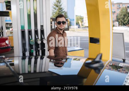 Gutaussehender Mann, der sein Luxusauto an einer Selbstbedienungstankstelle betankt. Benzinbefüllung an der Tankstelle im Auto mit einer Kraftstoffdüse. Stockfoto