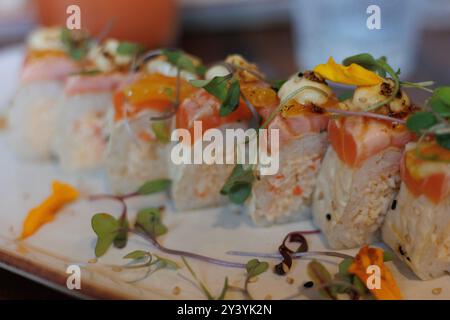 Eine Nahaufnahme einer Sushi-Spezialität mit gebratenem Lachs, scharfer Krabbe, Garnelentempura und Aioli, garniert mit Mikrogrün, mit lebendigem Co Stockfoto