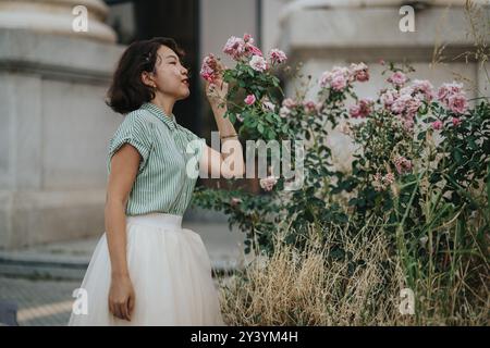 Frau, die blühende Blumen im Garten bewundert. Die Dame riecht rosa Rosen in urbaner Umgebung zur Entspannung Stockfoto