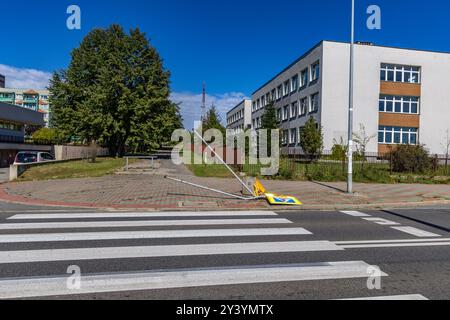 Verkehrsunfall auf den Fahrspuren neben einem markierten Fußgängerübergang zur Schule, beschädigtes Verkehrsschild, reflektierende Figur, die vor dem Fußgängerübergang warnt Stockfoto