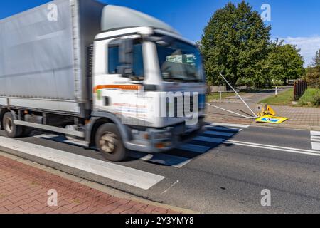 Verkehrsunfall auf den Fahrspuren neben einem markierten Fußgängerübergang zur Schule, beschädigtes Verkehrsschild, reflektierende Figur, die vor dem Fußgängerübergang warnt Stockfoto