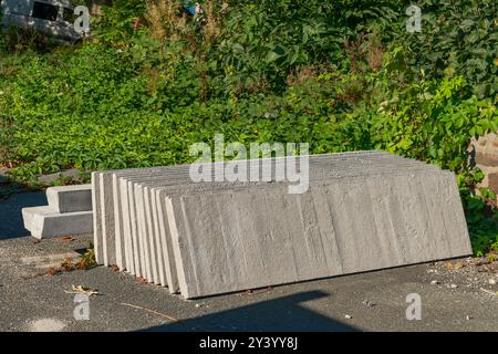 Mehrere Betonplatten liegen auf einer Kiesoberfläche, die tagsüber von grünem Laub umgeben ist, und weisen auf eine mögliche Bau- oder Landschaftsgestaltung hin Stockfoto