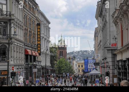 Geschäftige Einkaufsstraße mit mehreren Geschäften, im Hintergrund ein hügeliges Panorama und bewölkter Himmel, oslo, norwegen Stockfoto
