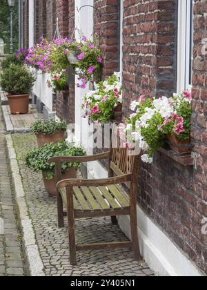 Eine rustikale Szene mit einer Holzbank und blühenden Fensterkästen entlang einer Backsteinmauer und Kopfsteinpflasterstraße, Huenxe, Niederrhein, Deutschland, Europa Stockfoto