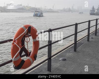 Rettungsschwimmer auf dem Geländer entlang eines Flusses. Boote im Hintergrund bei Nebel, Hamburg, Deutschland, Europa Stockfoto