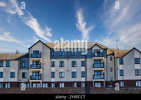 Ein modernes Apartmentgebäude mit einer Mischung aus grau und weiß. Das Gebäude verfügt über mehrere Balkone und große Fenster. Der Himmel darüber ist hell Stockfoto