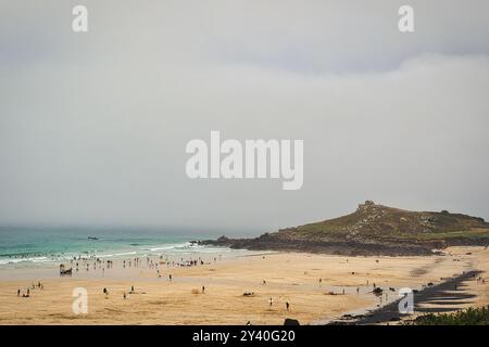 Ein malerischer Blick auf den Strand mit Leuten, die verschiedene Aktivitäten genießen. Die Sandküste ist von Strandgängern gespickt, während sanfte Wellen an der Küste herumplätschern. In Th Stockfoto