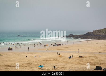 Eine bewölkte Strandszene mit Leuten, die verschiedene Aktivitäten genießen. Das Sandstrand ist gespickt mit Strandgängern, einige schwimmen im Meer, andere entspannen sich Stockfoto