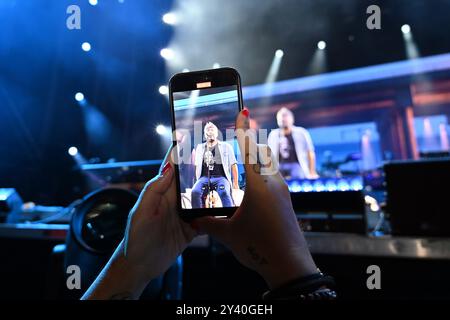 Tarragona, Spanien. September 2024. Eine Frau fotografiert Estopa-Sänger David Muñoz mit ihrem Smartphone während seines Auftritts. Die spanische Musikgruppe Estopa trat in Tarragona auf und feierte ihr 25-jähriges Bestehen vor einer ausverkauften Menschenmenge von 10.000 Fans im Anella Mediterranìa Complex (Foto: Ramon Costa/SOPA Images/SIPA USA) Credit: SIPA USA/Alamy Live News Stockfoto