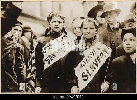 Protest gegen Kinderarbeit bei einer Arbeiterparade - Foto zeigt ein halblanges Porträt von zwei Mädchen, die Banner tragen mit dem Slogan „ABOSH CH[LD SKLAVEREI!!“ Auf Englisch und Jiddisch, einer mit amerikanischer Flagge; Zuschauer stehen in der Nähe. Wahrscheinlich während der Arbeiterparade am 1. Mai 1909 in New York City. Stockfoto