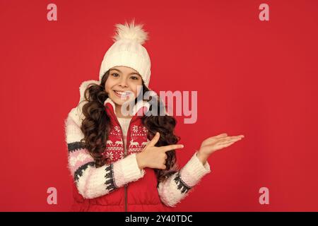 Frohes jugendliches Mädchen auf rotem Hintergrund. Porträt des Kindes trägt warme Kleidung. positive Emotion ausdrücken. Stockfoto