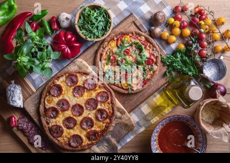 Pizza mit Salami, Käse, Soße, Tomaten, Gemüse und frischen Kräutern auf hölzernem Hintergrund. Draufsicht Stockfoto