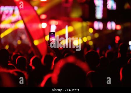 Bühnenlichter als Unschärfe-Bokeh-Hintergrund bei einem Musikkonzert und Hand mit Smartphone-Video, das die Live-Show aufzeichnet Stockfoto