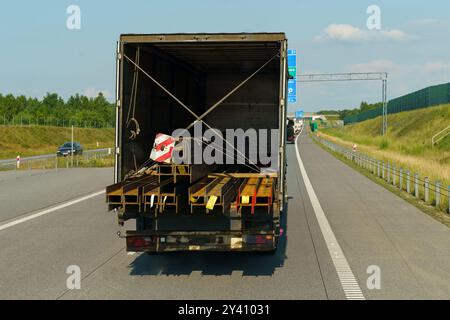 Ein großer Lkw, gefüllt mit Metallbalken und Materialien, fährt auf einer sonnigen, von Grün umgebenen Autobahn und hebt den Warenfluss auf stark frequentierten Trans hervor Stockfoto