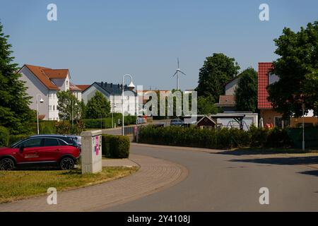 Waltershausen, Deutschland - 11. Juni 2023: An einem ruhigen Sommernachmittag in Waltershausen säumen Häuser die Straßen, während sich Windräder sanft unter einem drehen Stockfoto