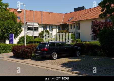 Waltershausen, Deutschland - 11. Juni 2023: Unter klarem blauen Himmel parkt ein schwarzes Auto neben charmanten Gebäuden, umgeben von grünen Sträuchern und Colo Stockfoto