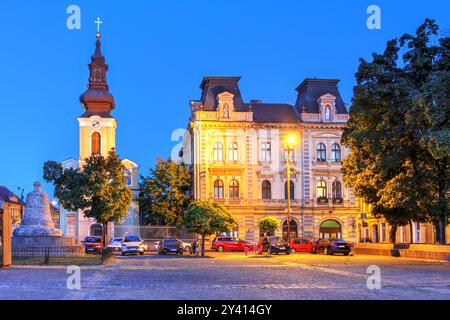 Nacht in Piata Traian (Traian-Platz) in Timisoara, Rumänien mit der St. Georgskirche und dem Palast der serbischen Gemeinde. Stockfoto