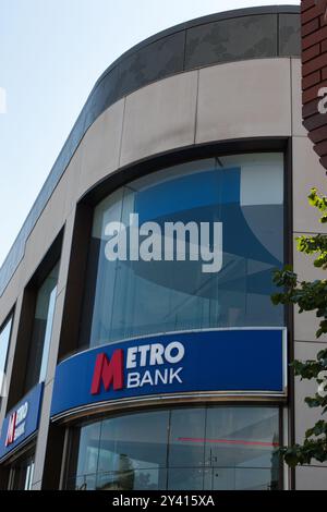 Ein modernes Bankgebäude mit großen Glasfenstern und einem auffälligen blau-roten Schild mit dem Namen „Metro Bank“. Die Architektur verfügt über einen geschwungenen Stockfoto