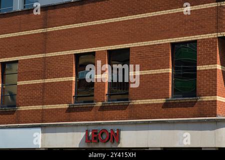 Aus nächster Nähe eine Backsteinfassade mit großen Fenstern. Das Gebäude hat ein rotes Backsteingebäude mit weißen horizontalen Streifen. Das Wort „LEO Stockfoto