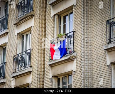 Typische Pariser Gebäudefassade mit französischer Flagge auf dem Balkon. Typisches Gebäude in Paris, Frankreich. Stockfoto