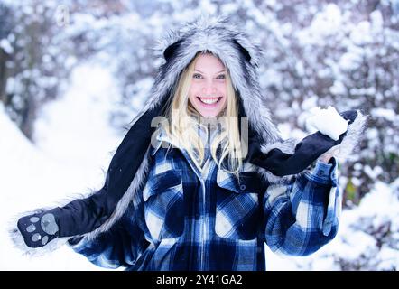 Winterzeit. Lächelnde Frau, die im Winterpark mit Schnee spielt. Verspieltes Mädchen in warmer Kleidung mit Schneeball. Winterurlaub Aktivität. Glückliches Mädchen mit f Stockfoto