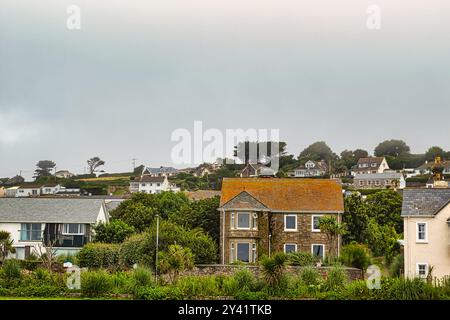 Ein malerischer Blick auf ein Küstendorf mit verschiedenen Häusern, einschließlich eines Steinhauses mit einem orangen Dach, umgeben von Grün und Hügeln unter einem bewölkten s Stockfoto