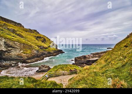 Ein malerischer Blick auf die Küste mit felsigen Klippen, üppigen grünen Hügeln und einem Sandstrand. Die Meereswellen krachen unter bewölktem Himmel gegen die Küste, Kreatin Stockfoto