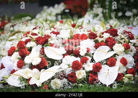 Trauerblumen aus roten Rosen und Nelken und weißen Gerbera- und Flamingoblumen und gypsophila auf einem Grab nach einer Beerdigung Stockfoto