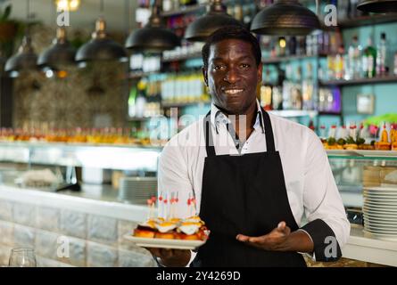 Blick auf den erwachsenen afrikanischen Mann, der in einem Pub Tapas hält Stockfoto