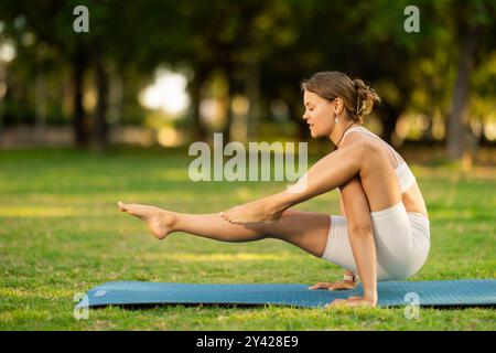 Sportliches Mädchen, das einen Arm ausbalanciert, Elephant Trunk-Pose im Sommerpark Stockfoto