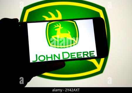 In dieser Fotoabbildung wird ein John deere-Logo auf einem Smartphone und im Hintergrund angezeigt. Stockfoto