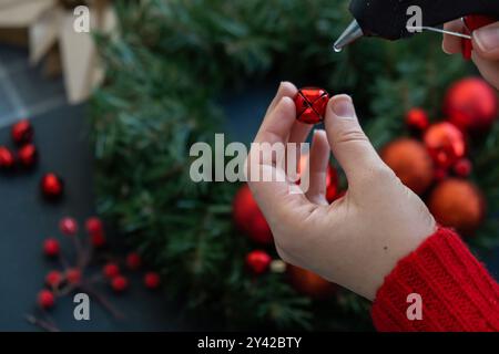 Crafter mit heißem Leim Schritt für Schritt Anleitung zur Herstellung von handgefertigten Weihnachtskranz aus festlichen Dekorationen in roter Farbe. Weibliche Hände kreieren hausgemachte Kreationen. Neujahrsfeier. Winterferien Schritt 2 Stockfoto