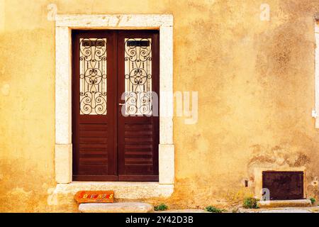 Alte braune Holztür mit Verzierung an der gelben Wand. Stockfoto