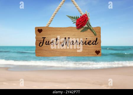 Flitterwochen. Holzbrett mit Worten, die gerade geheiratet wurden, und Boutonniere am Sandstrand Stockfoto