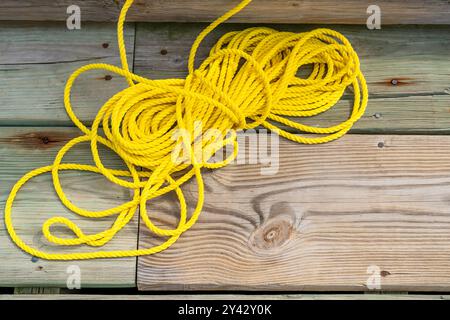 Gelbes Nylonseil, verbunden mit einem orangefarbenen Rettungsring, sitzend auf einem hölzernen Dock, Pier. Stockfoto