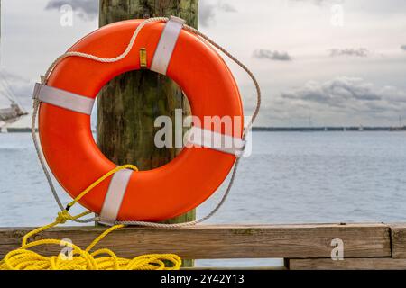 Orangefarbener Rettungsring, Hafenlebensretter, montiert auf einem Dockenstapel mit einem gelben Nylonseil. Stockfoto