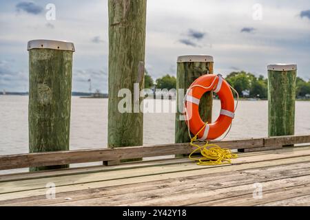 Orangefarbener Rettungsring, Hafenlebensretter, montiert auf einem Dockenstapel mit einem gelben Nylonseil. Stockfoto